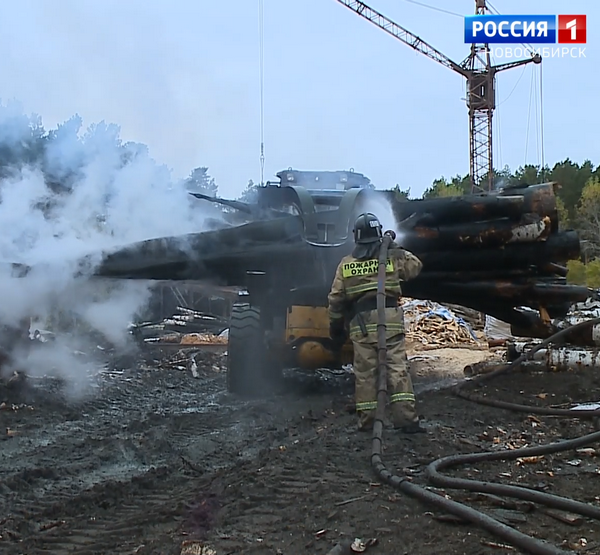 Пожарный проливает тлеющие брёвна, вывезенные погрузчиком