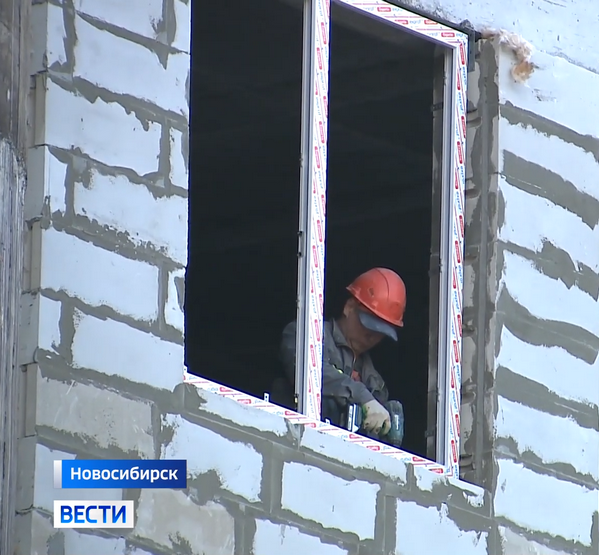 Рабочий монтирует раму окна